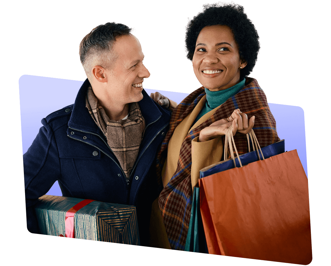 A smiling couple with the man holding a present and the woman holding several shopping bags